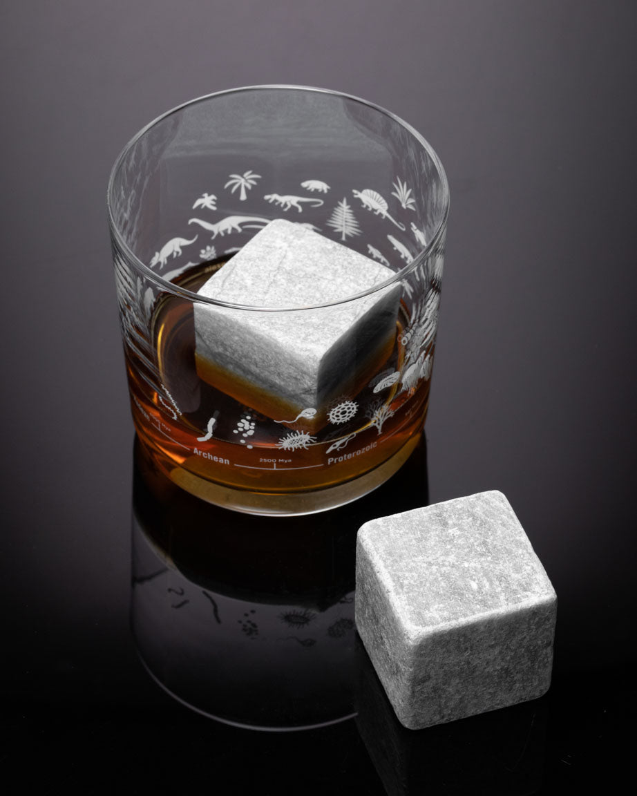 Two Mega Rocks Soapstone Whiskey Stones next to a glass of whiskey from Cognitive Surplus.